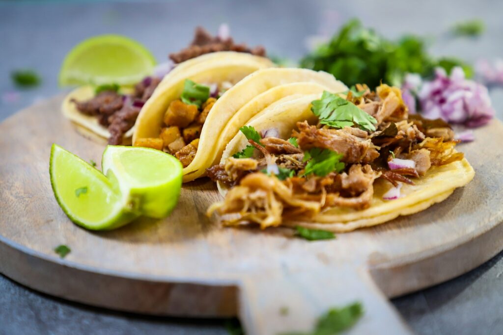 Wooden plate topped with three tacos and a lime